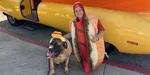 Person with a dog smiling in front of the Wienermobile.