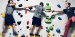 Three guys on a climbing wall holding hands.