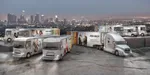 Several big trucks parked in front of a city skyline.