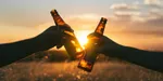 2 hands in sunset tapping beerbottles together.